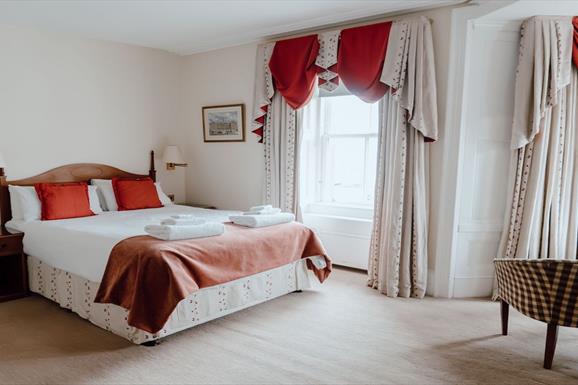 A cosy hotel room with a comfortable bed, a chair, and a window offering a scenic view.